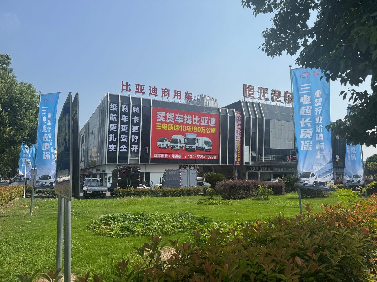客户场地实景：园区正门展车区，草坪旁停放多辆展车，两侧竖立品牌道旗